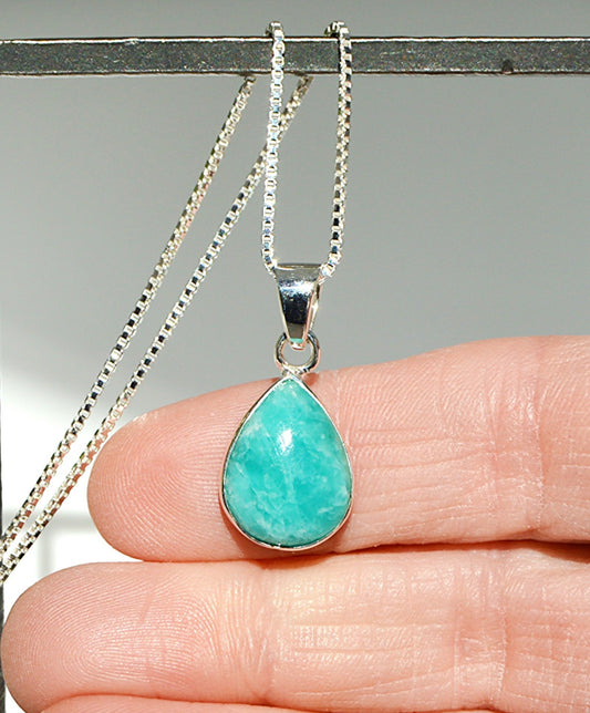 Turquoise teardrop pendant on a silver chain held between fingers