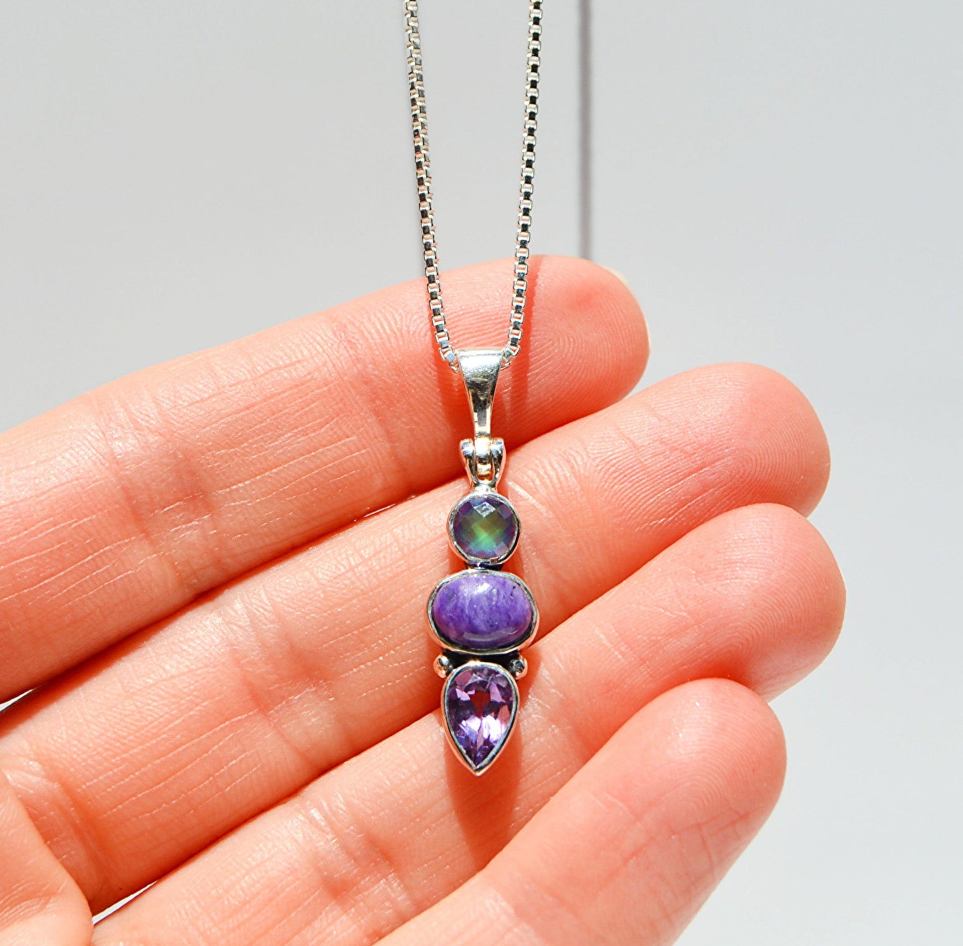 JeniMarie Jewelry with a purple pendant with multiple stones with a box chain necklace. 