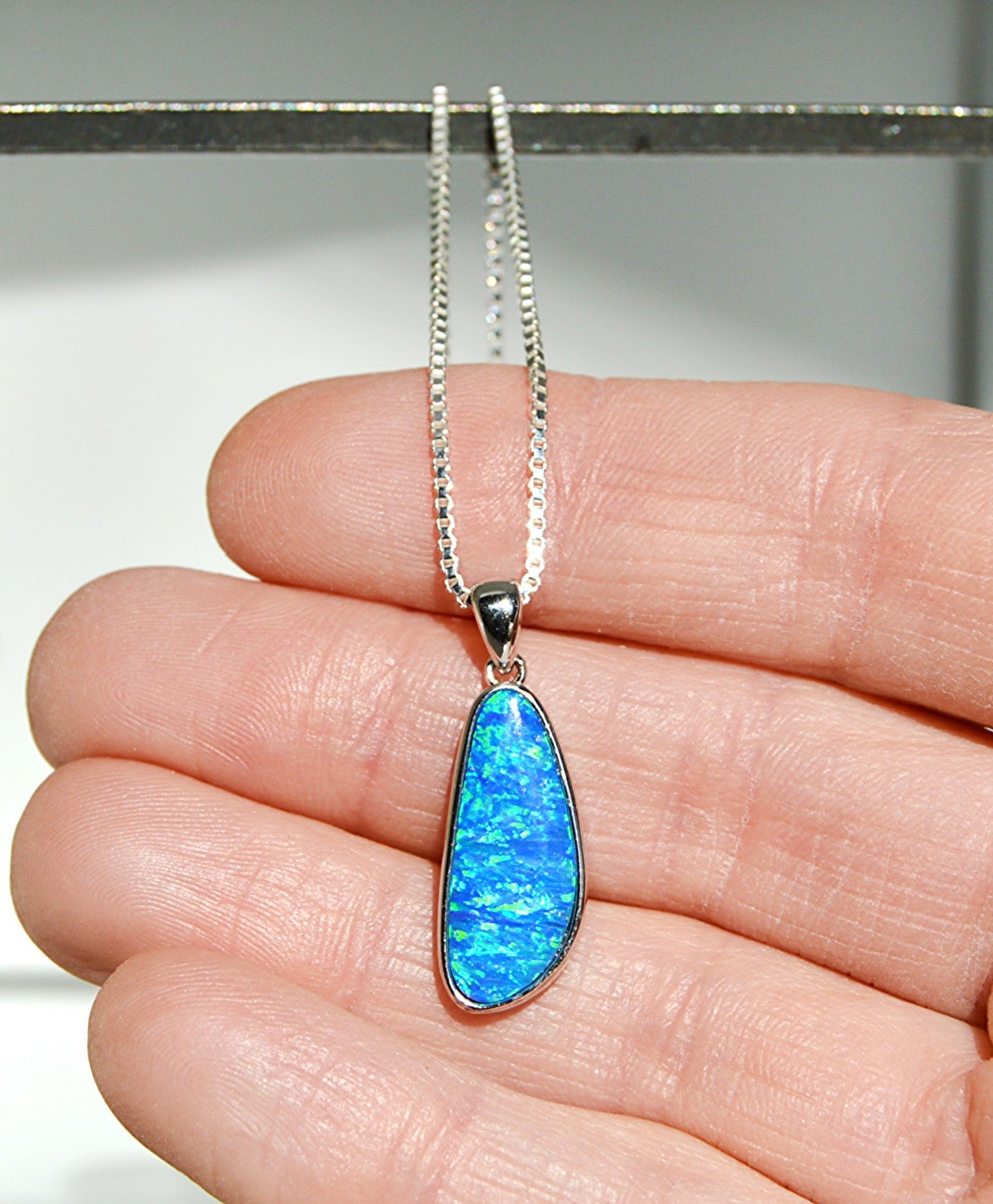 Blue opal pendant on a silver chain held between fingers