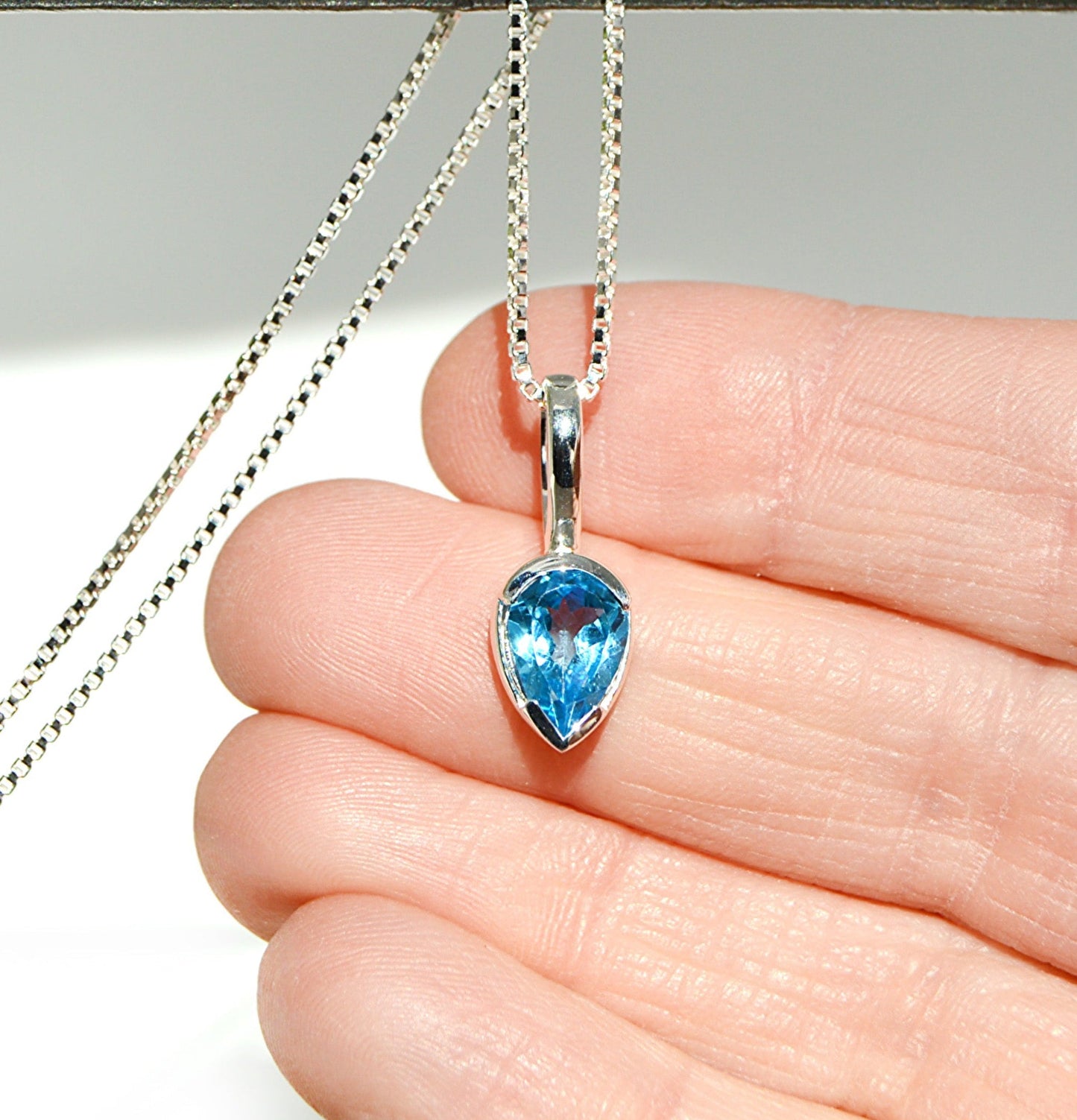 Blue teardrop pendant on a silver chain held between fingers