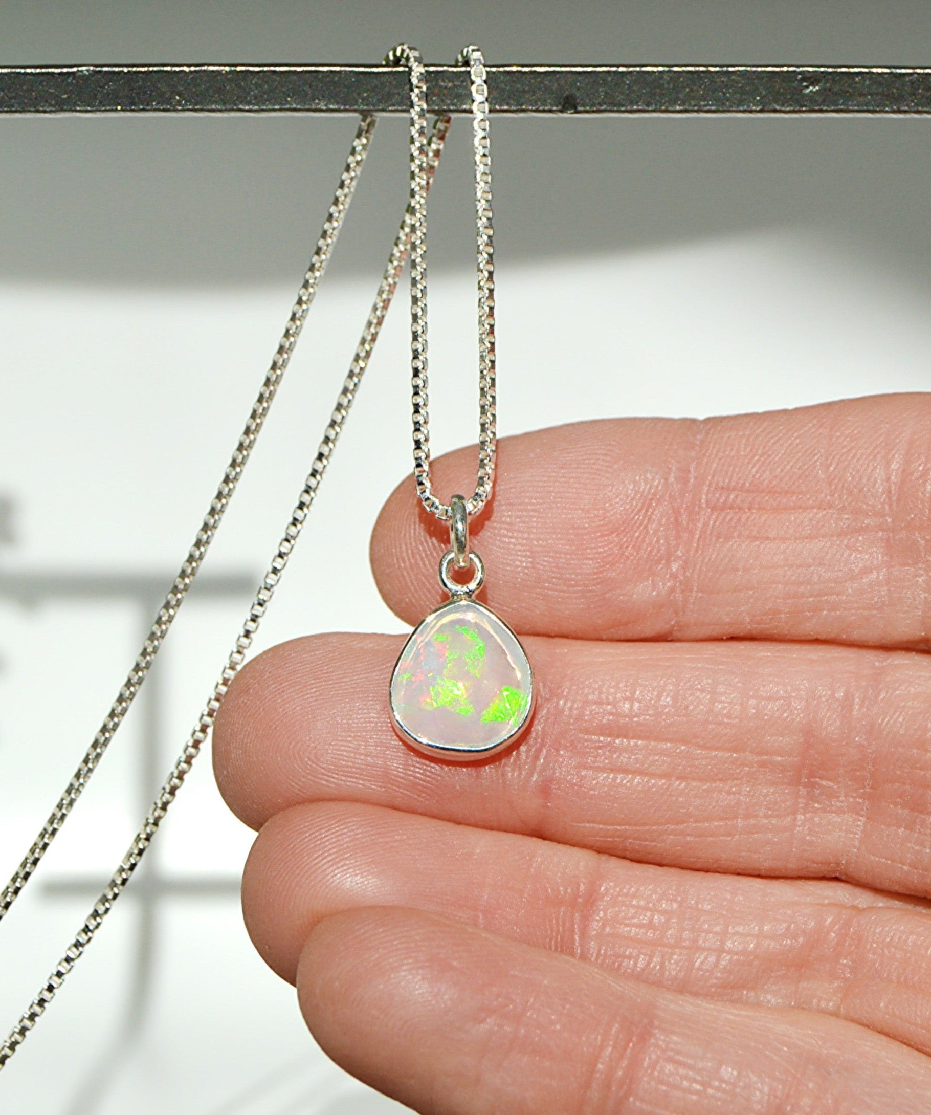 Necklace with a teardrop-shaped opal pendant held between fingers 