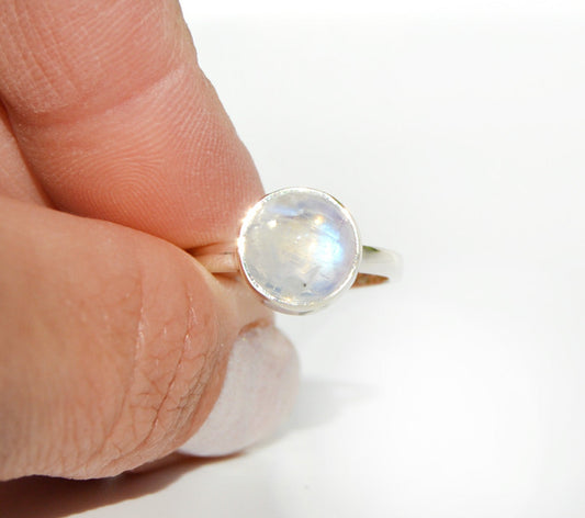 Silver ring with a moonstone held between fingers on a white background