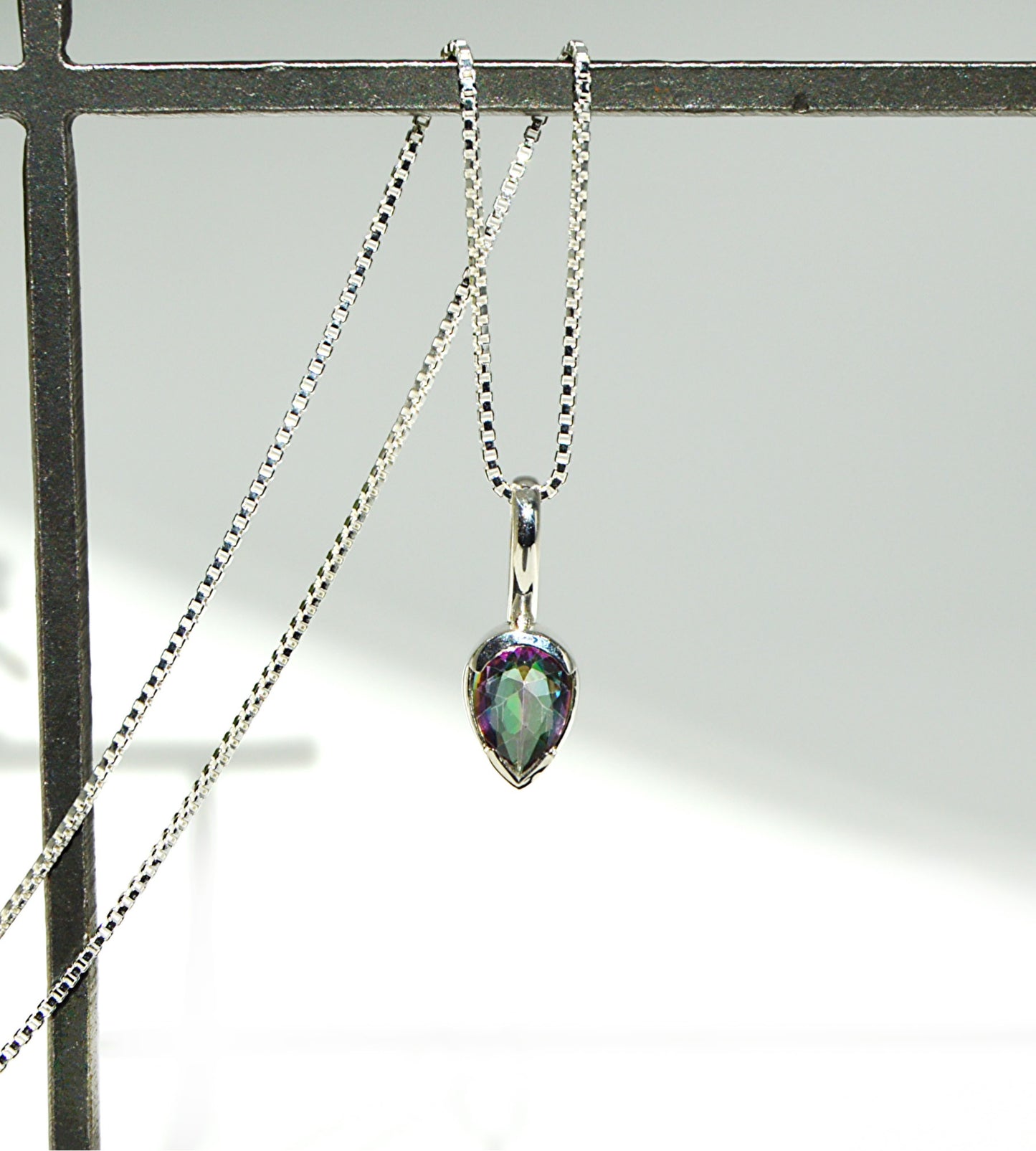 Teardrop-shaped pendant on a chain against a neutral background
