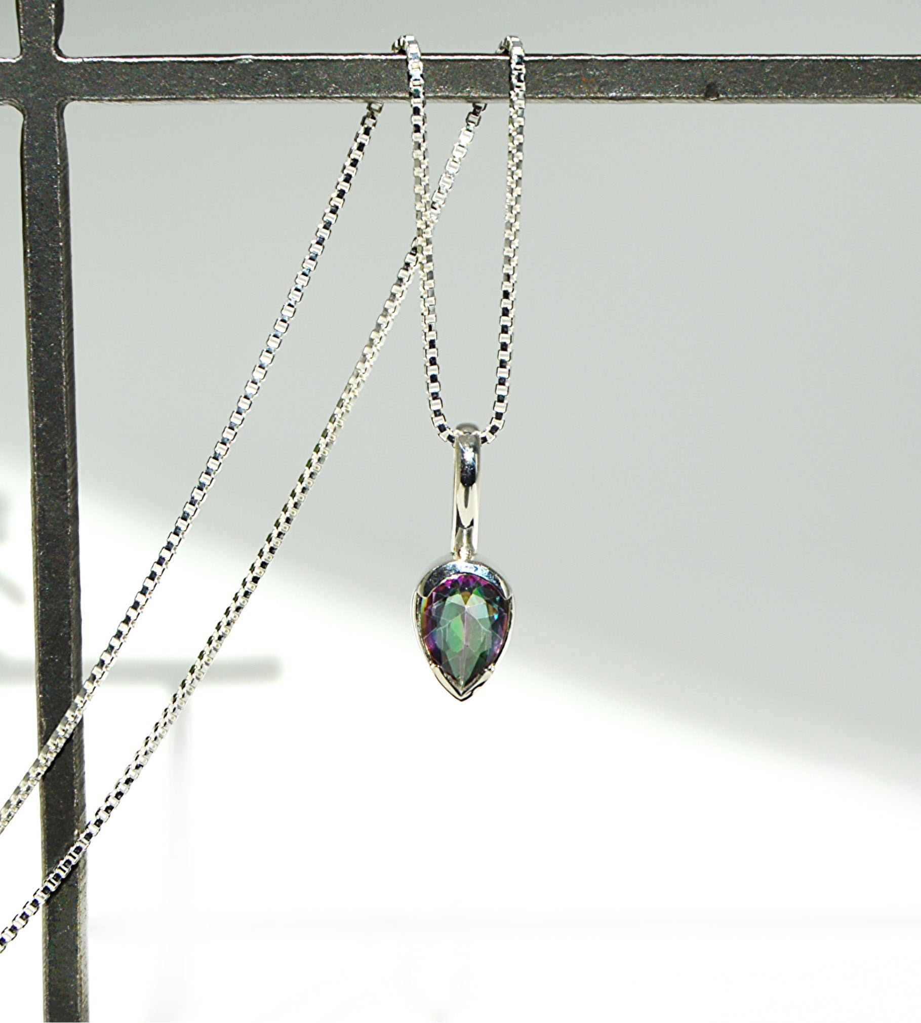 Teardrop-shaped pendant on a chain against a neutral background